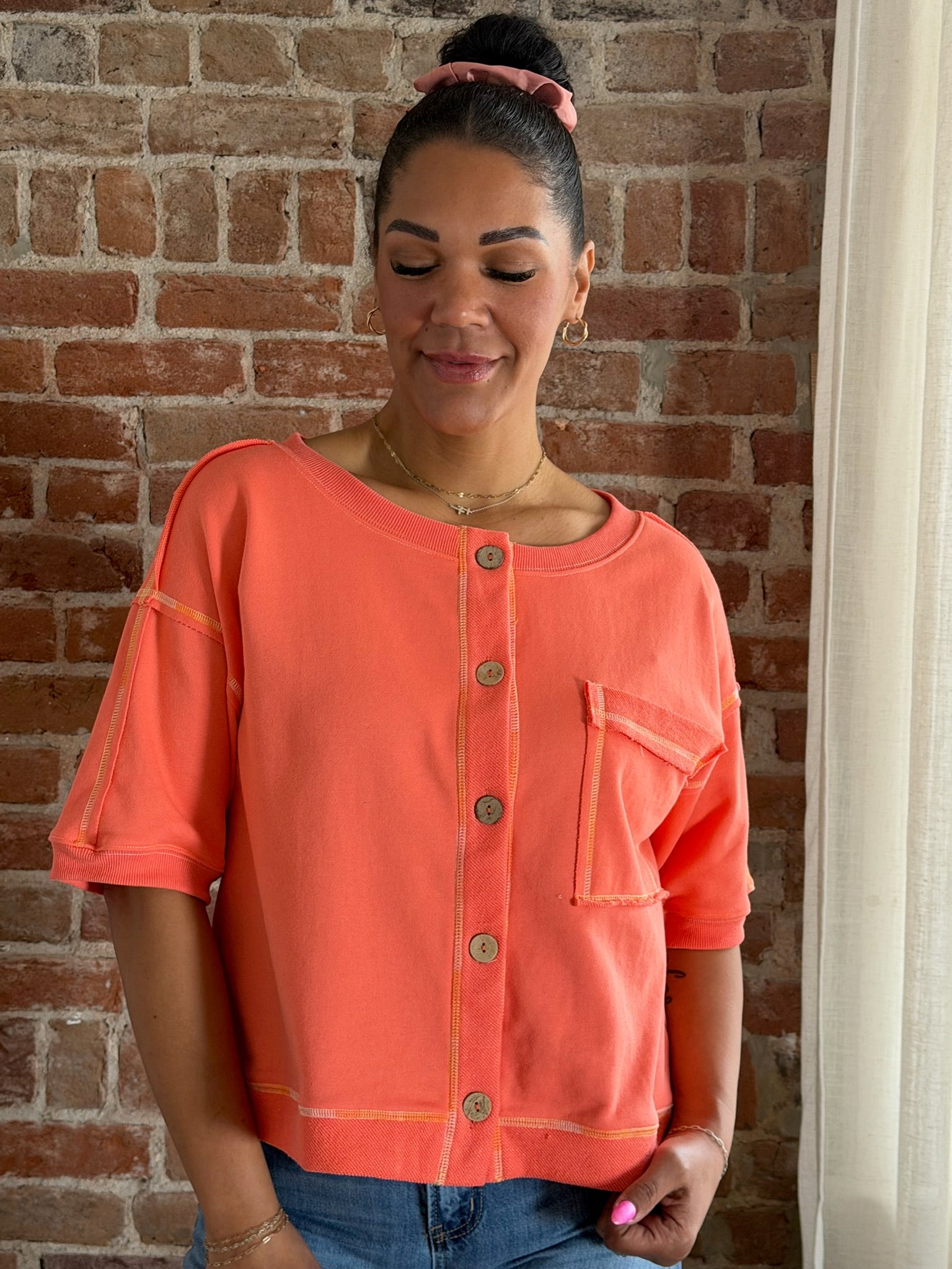 Woman wearing an orange button-up shirt against a brick wall