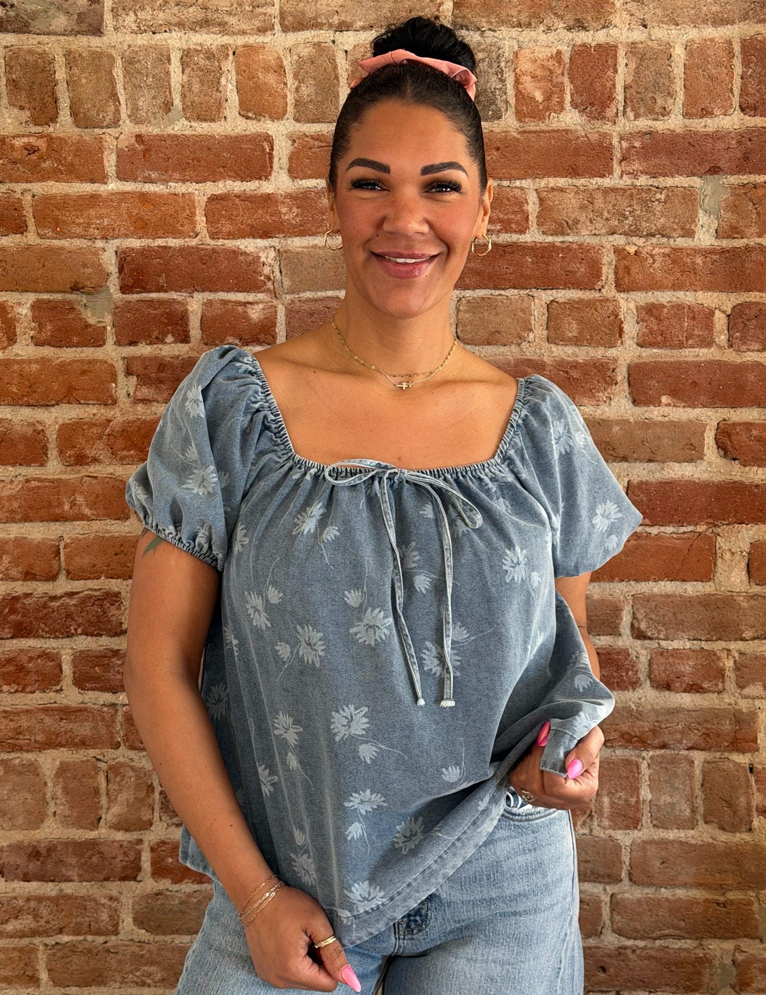 Woman wearing a blue floral blouse against a brick wall