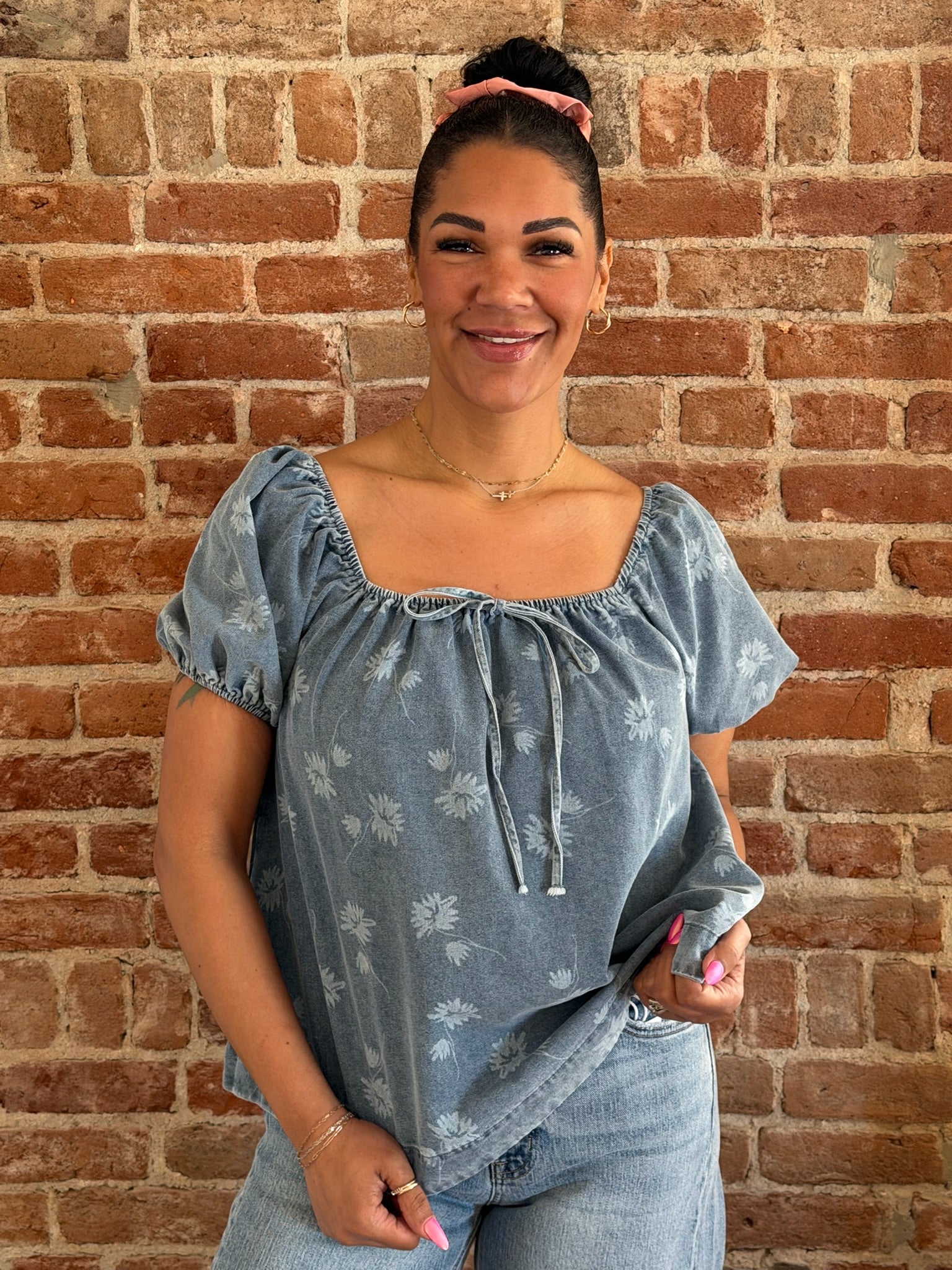 Woman wearing a blue floral blouse against a brick wall