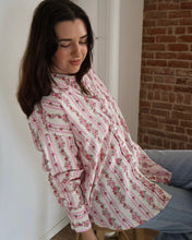 Woman wearing a floral blouse sitting against a brick wall.