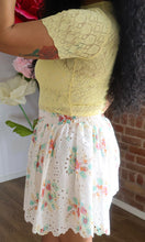 Person wearing a yellow lace top and floral skirt with a blurred background