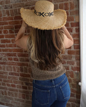 Person wearing a straw hat with a black band against a brick wall