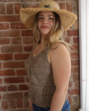 Woman wearing a straw hat and patterned tank top against a brick wall.