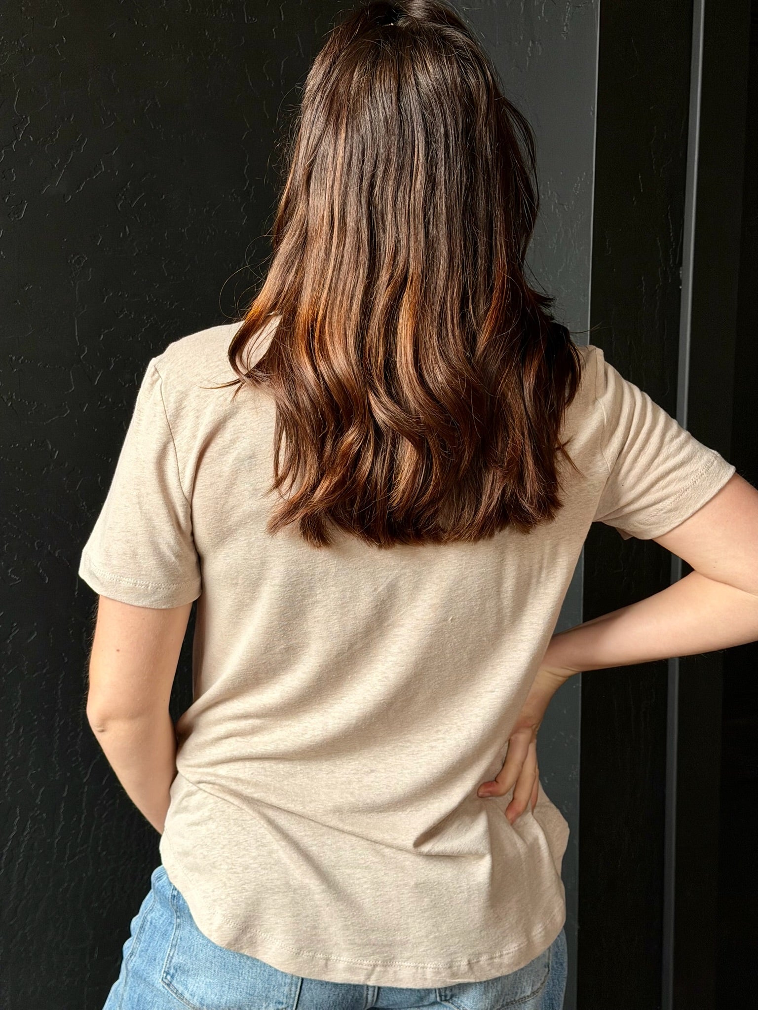 Person wearing a beige t-shirt and blue jeans against a black background