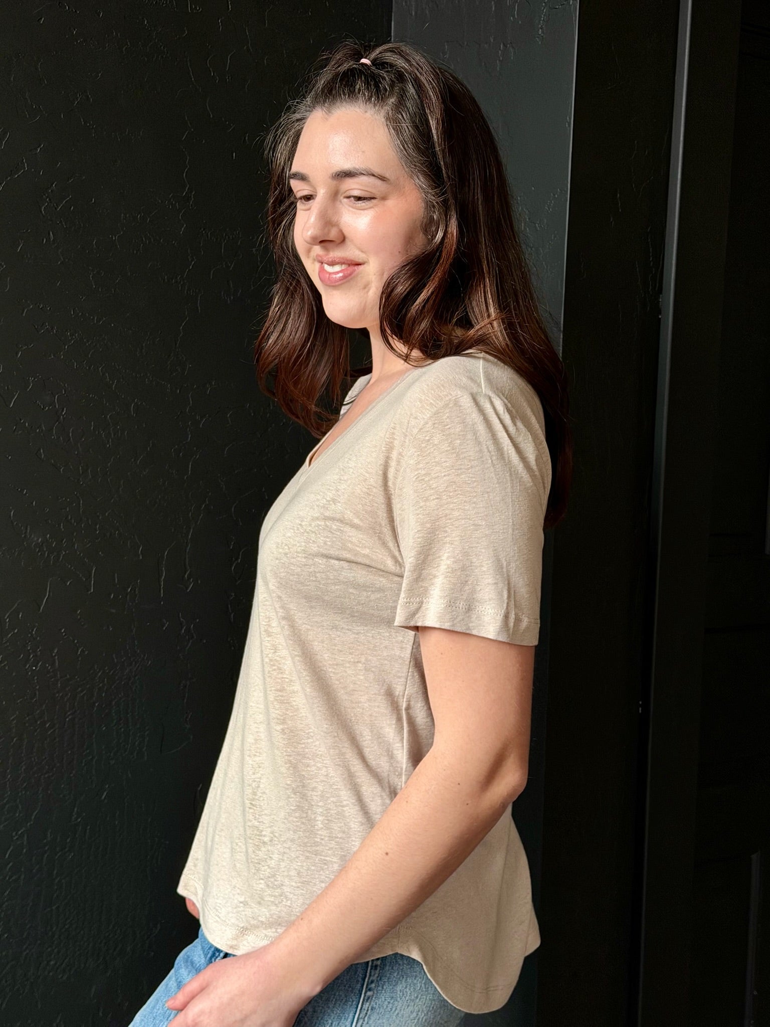 Woman wearing a beige t-shirt and blue jeans against a black background