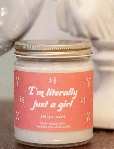 Candle with a pink label reading 'I'm literally just a girl' on a blurred background