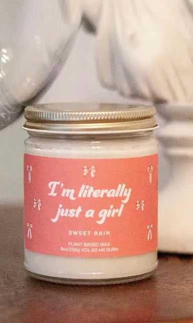 Candle with a pink label reading 'I'm literally just a girl' on a blurred background