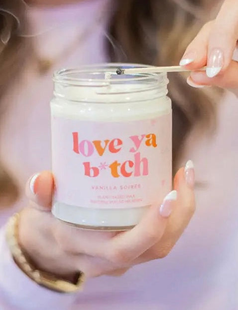 Person holding a candle labeled 'love ya b*tch' with a blurred background
