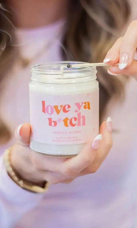 Person holding a candle labeled 'love ya b*tch' with a blurred background