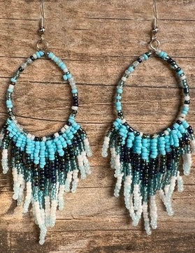 Beaded earrings with blue, black, and white fringes on a wooden surface