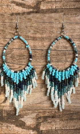 Beaded earrings with blue, black, and white fringes on a wooden surface