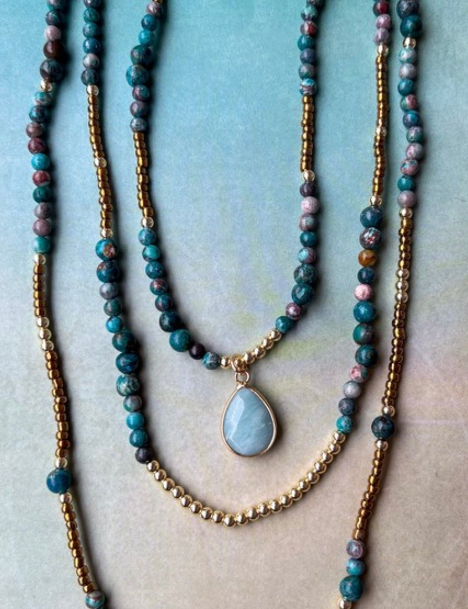 Stack of beaded necklaces with a pendant on a textured surface