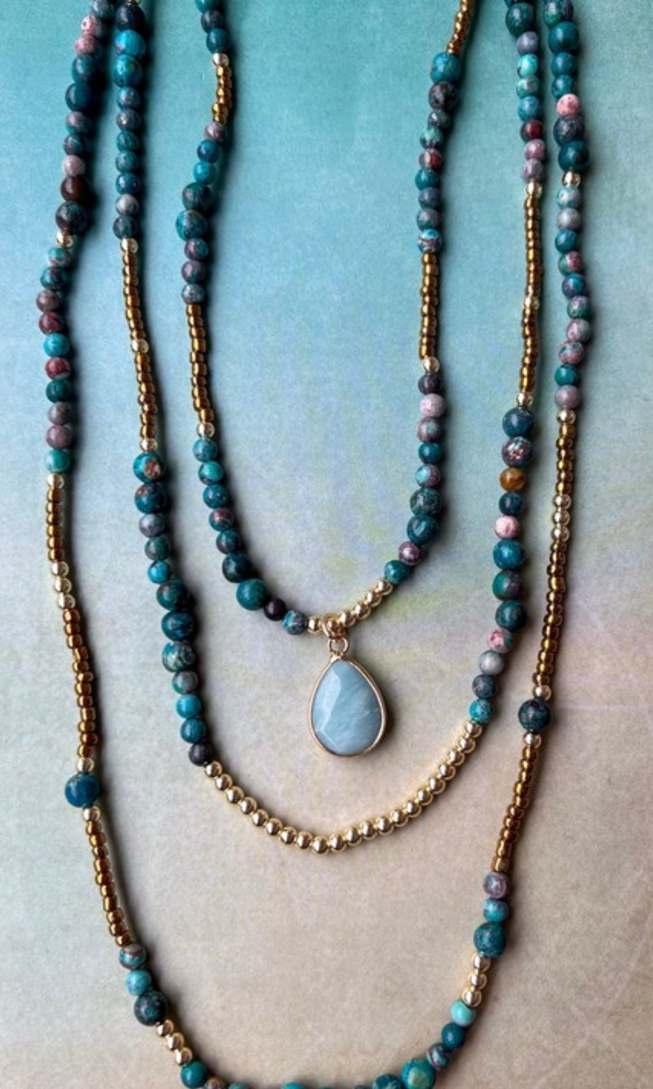 Stack of beaded necklaces with a pendant on a textured surface