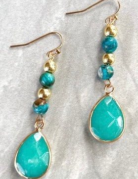 Turquoise teardrop earrings with gold beads on a textured white surface