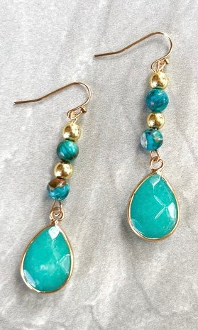 Turquoise teardrop earrings with gold beads on a textured white surface