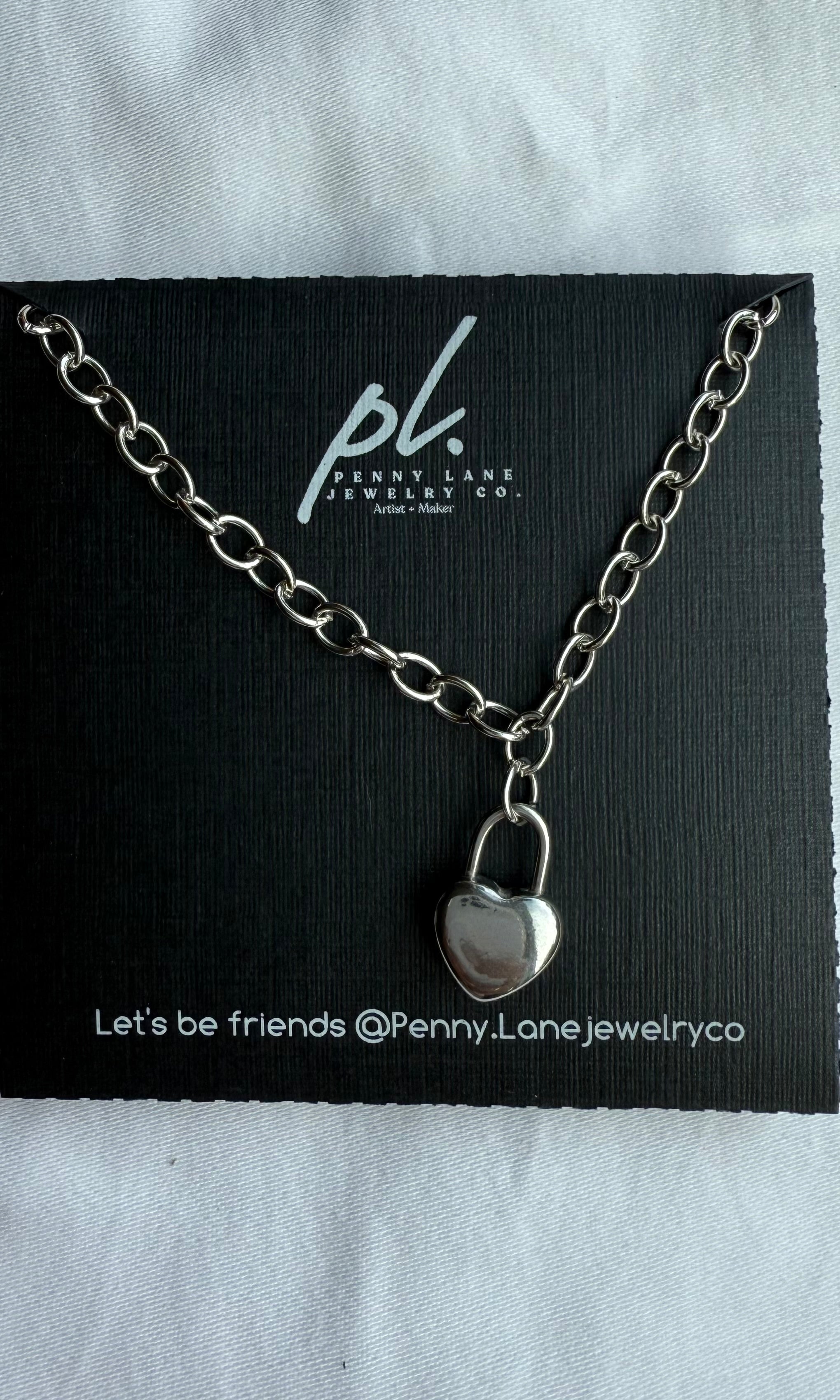Silver necklace with a lock pendant on a Penny Lane Jewelry Co card.