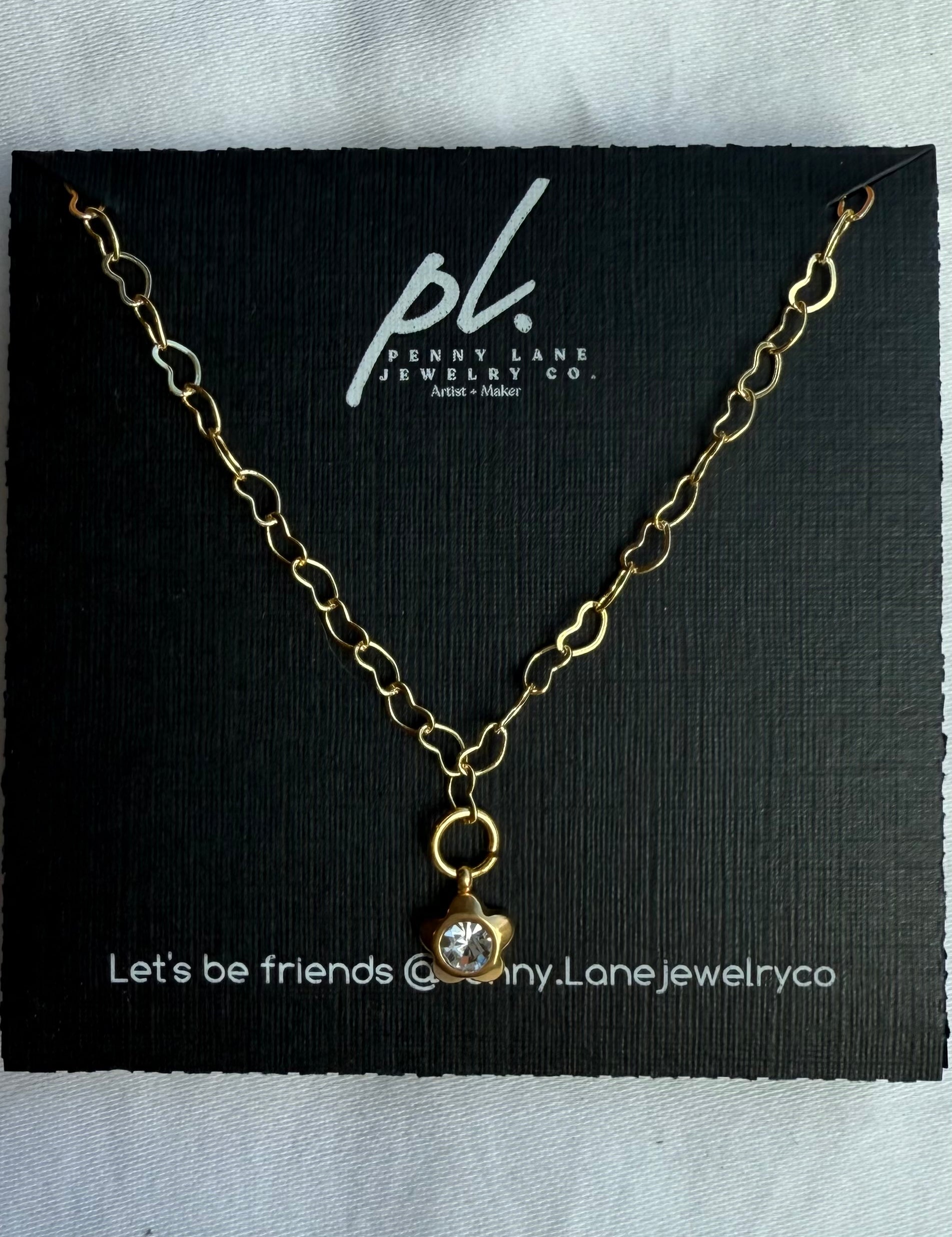 Gold necklace with a pendant on a black card featuring 'Penny Lane Jewelry Co.'