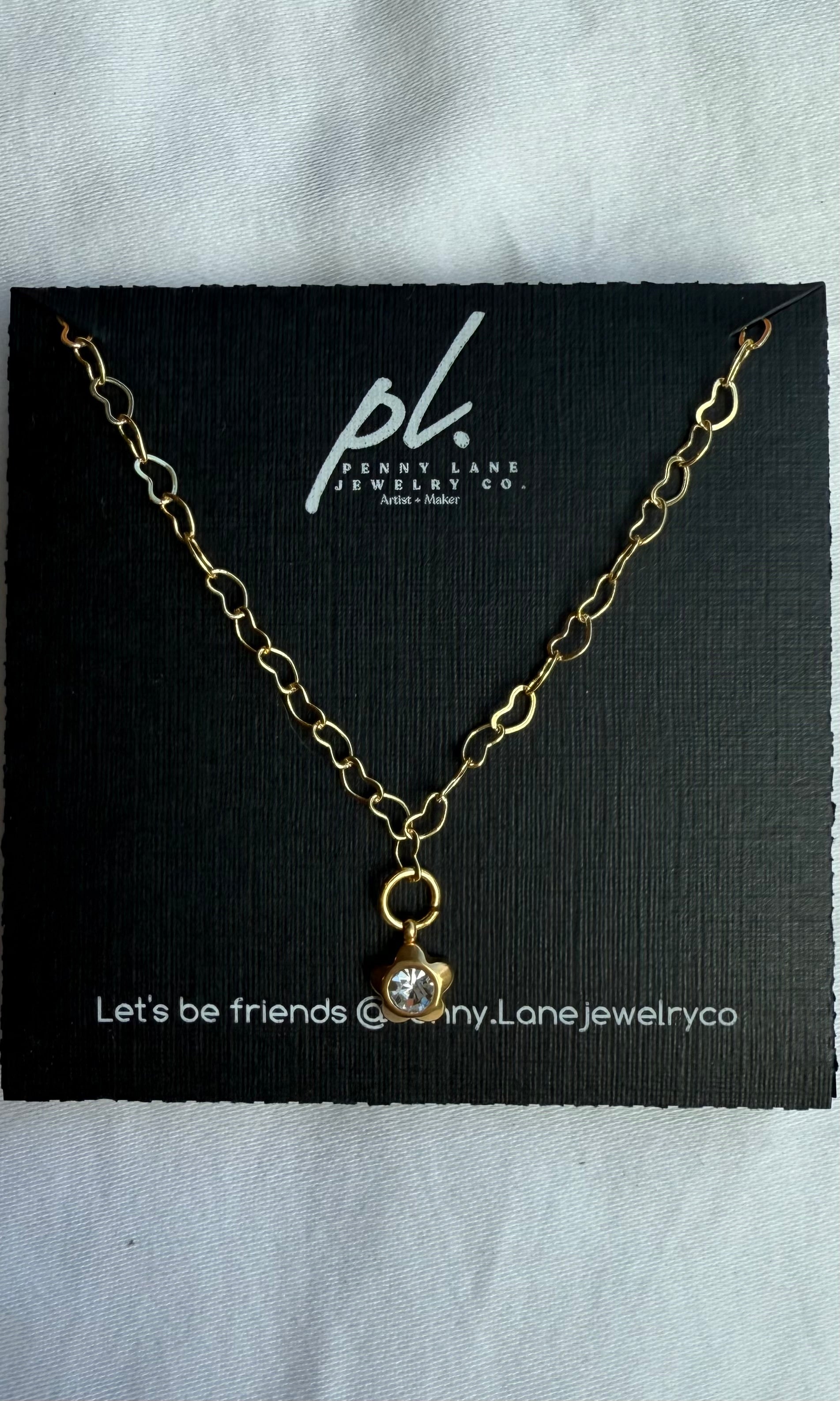 Gold necklace with a pendant on a black card featuring 'Penny Lane Jewelry Co.'