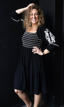 Woman wearing a black dress with white embroidery against a dark background