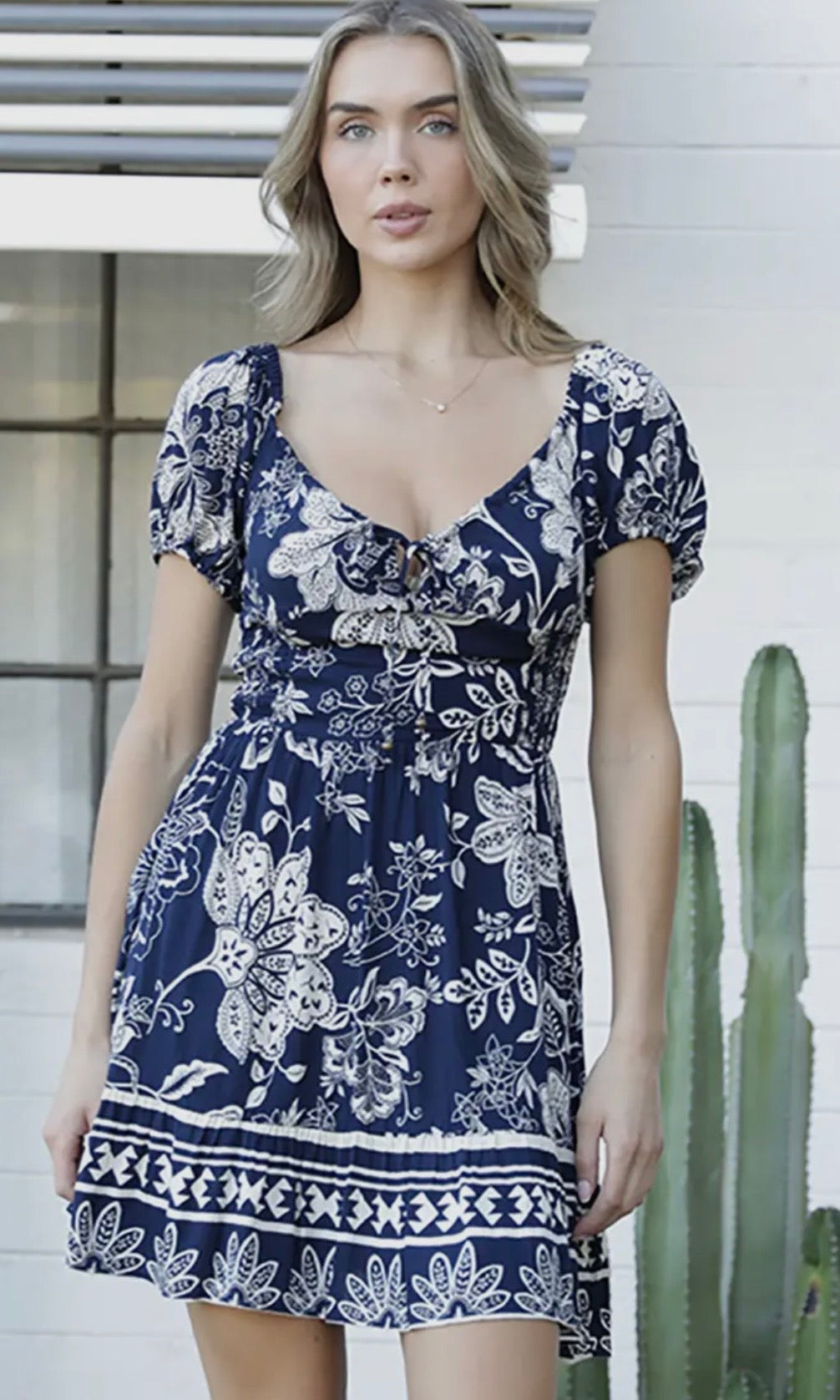 Woman wearing a navy blue dress with white floral patterns standing outdoors.