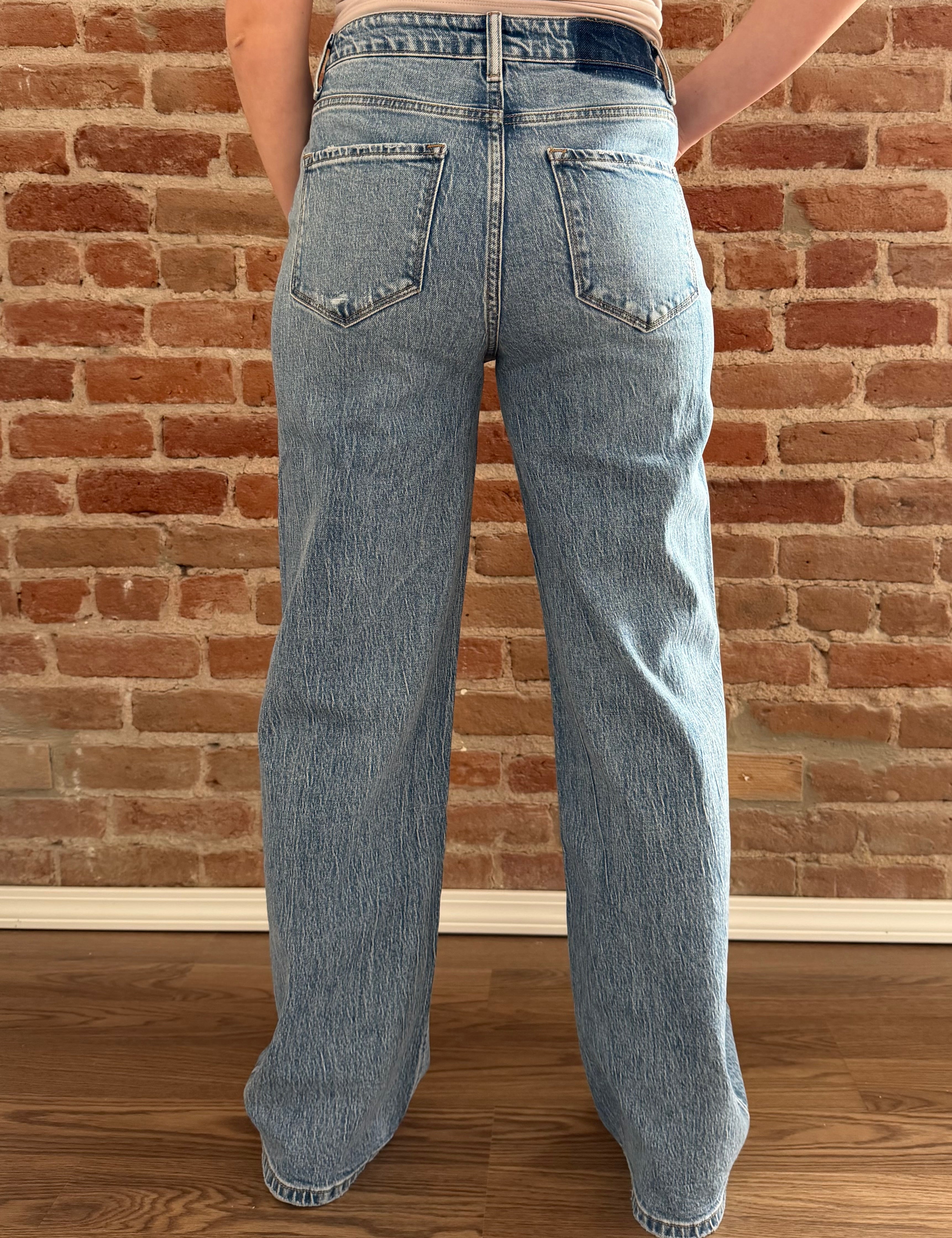 Person wearing light blue jeans standing against a brick wall.