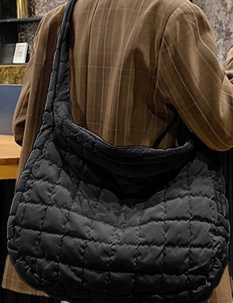 Person wearing a black quilted bag over one shoulder indoors.