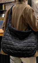 Person wearing a black quilted bag over one shoulder indoors.