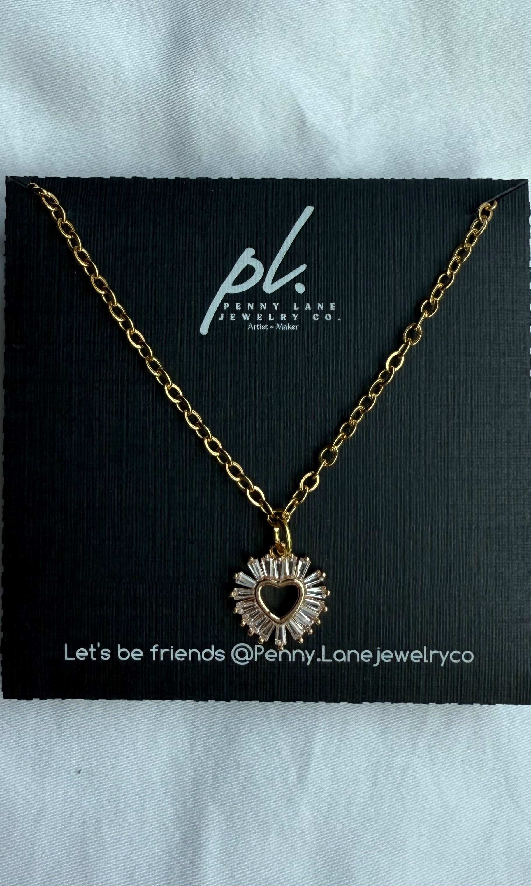 Gold necklace with a heart-shaped pendant on a Penny Lane Jewelry Co. card.