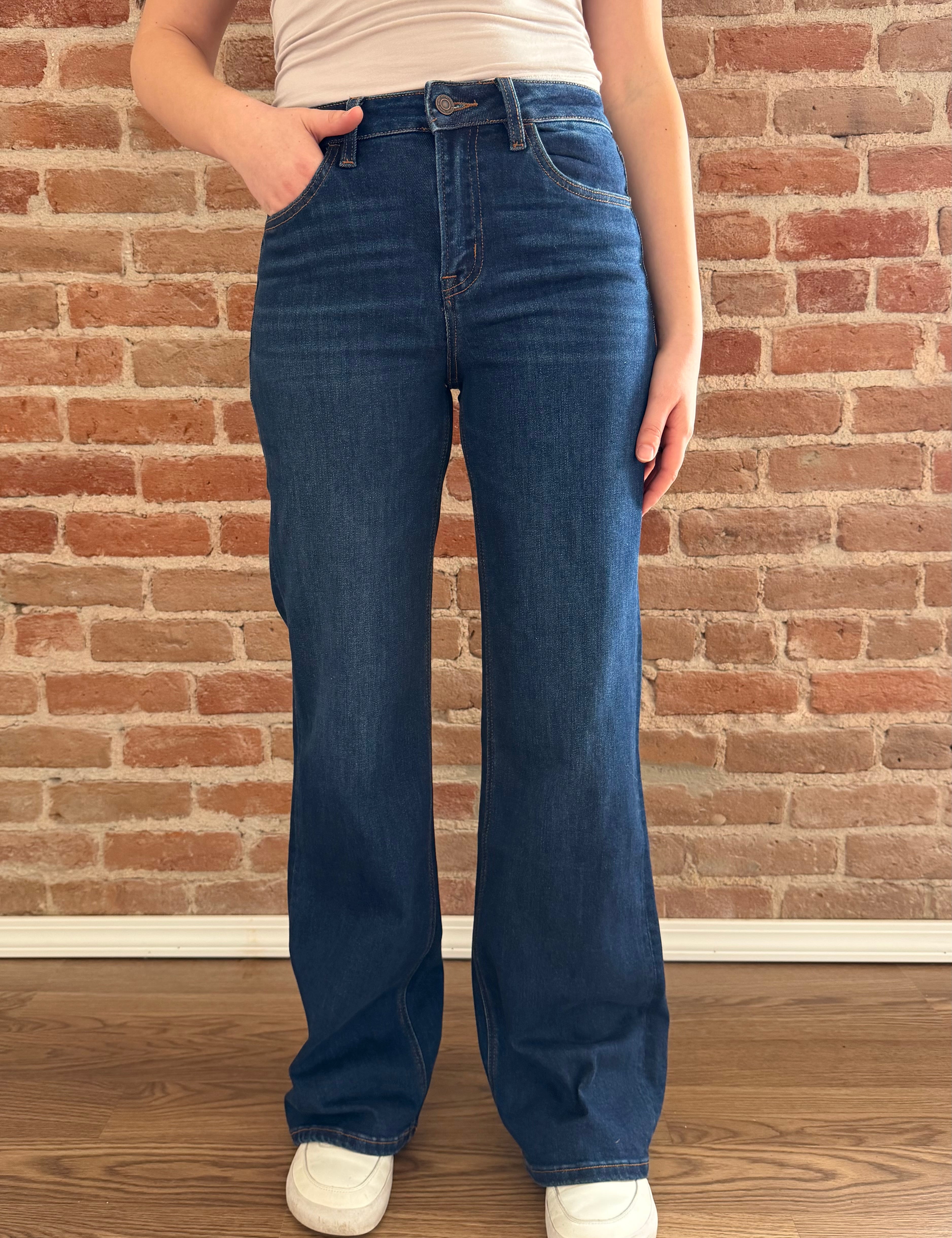 Person wearing blue jeans standing against a brick wall.