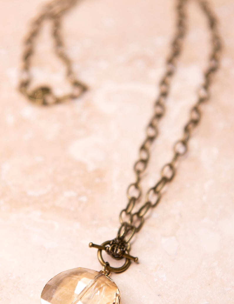 A brass chain-link necklace with a round shaped faceted glass pendant in a chain of faceted glass pendants.