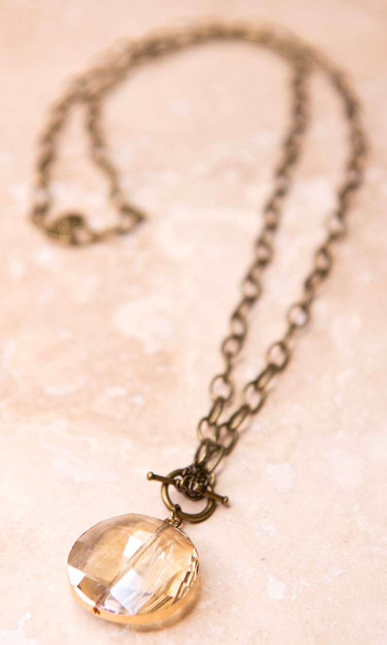 A brass chain-link necklace with a round shaped faceted glass pendant in a chain of faceted glass pendants.