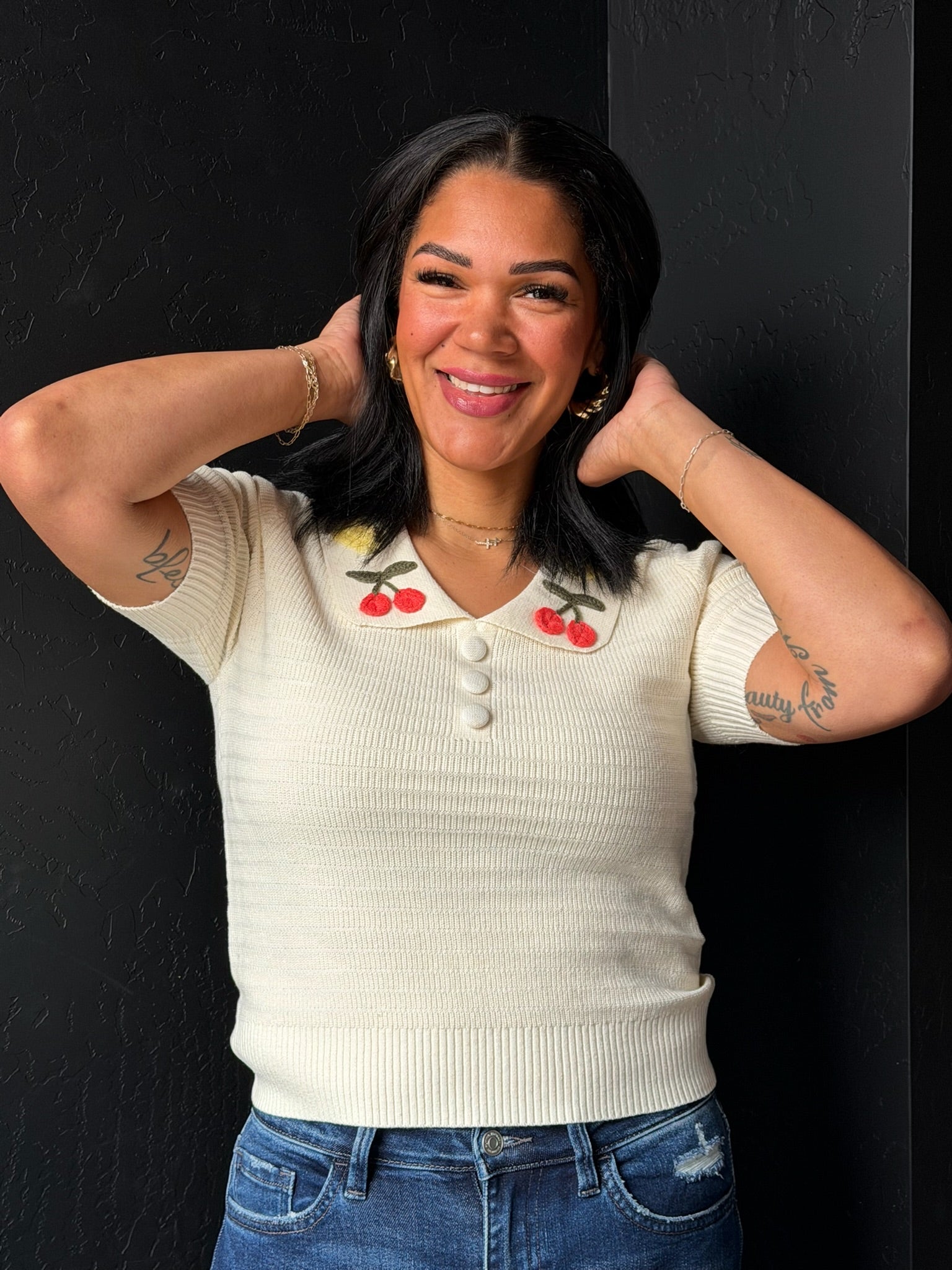 Woman wearing a cream-colored sweater with cherry designs on a black background