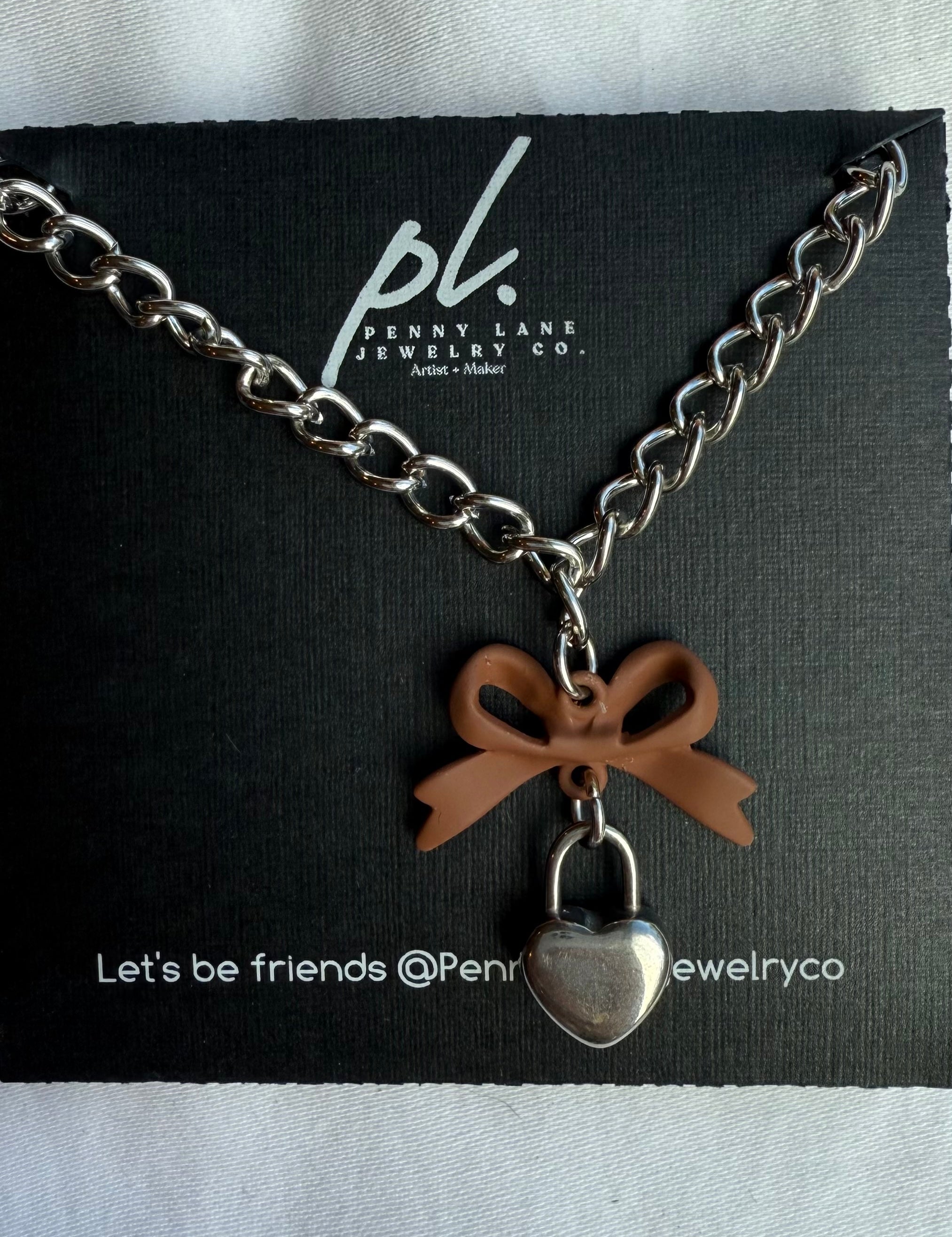 Necklace with heart-shaped pendant and bow charm on a Penny Lane Jewelry Co. card.