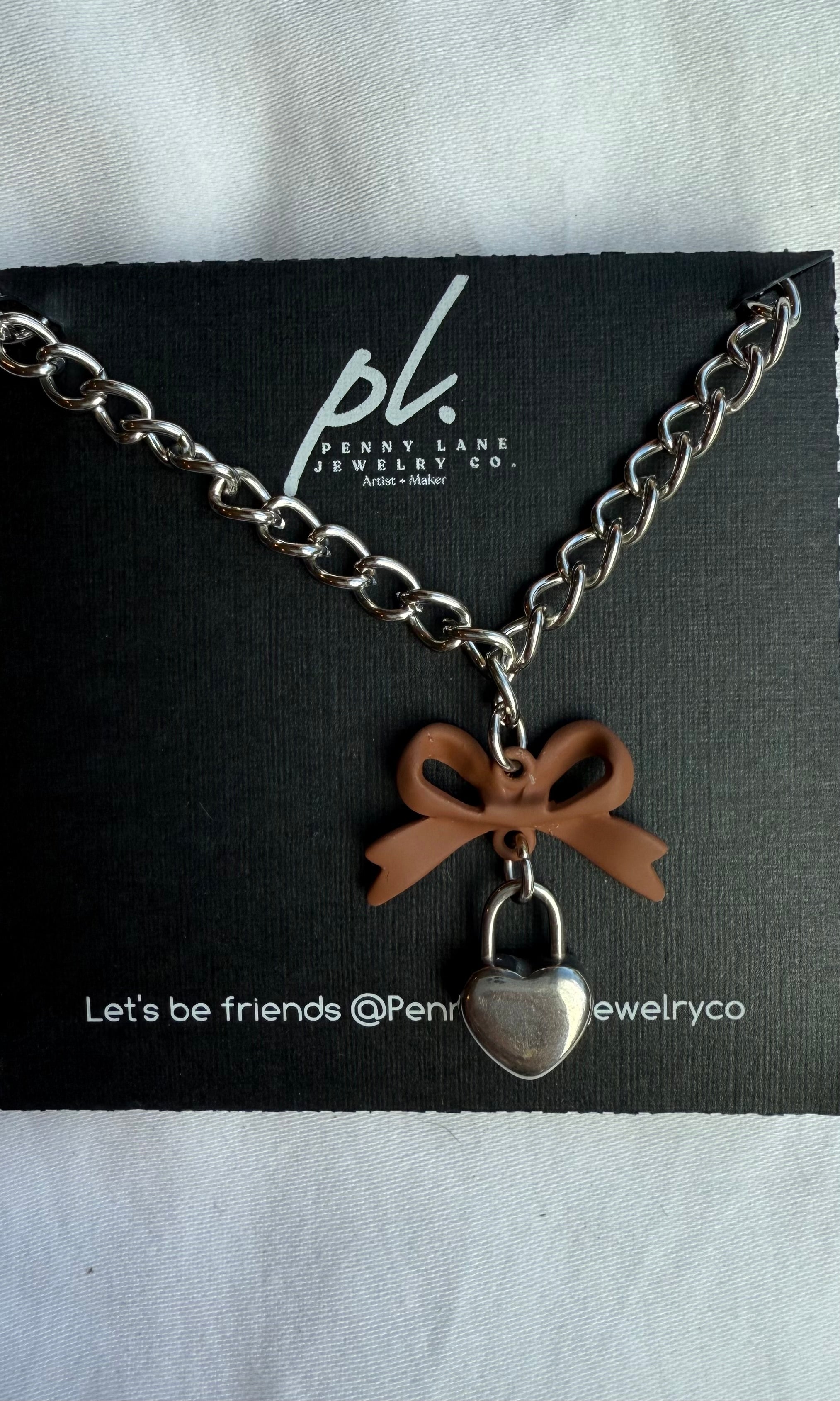 Necklace with heart-shaped pendant and bow charm on a Penny Lane Jewelry Co. card.