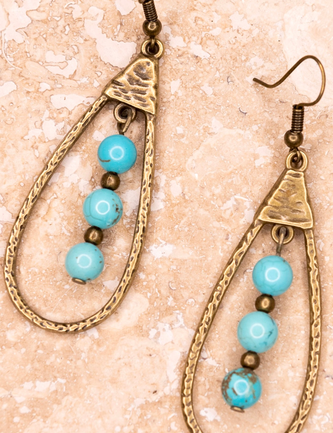 A pair of bronze teardrop-shaped dangle earrings with turquoise beads and brown accents.
