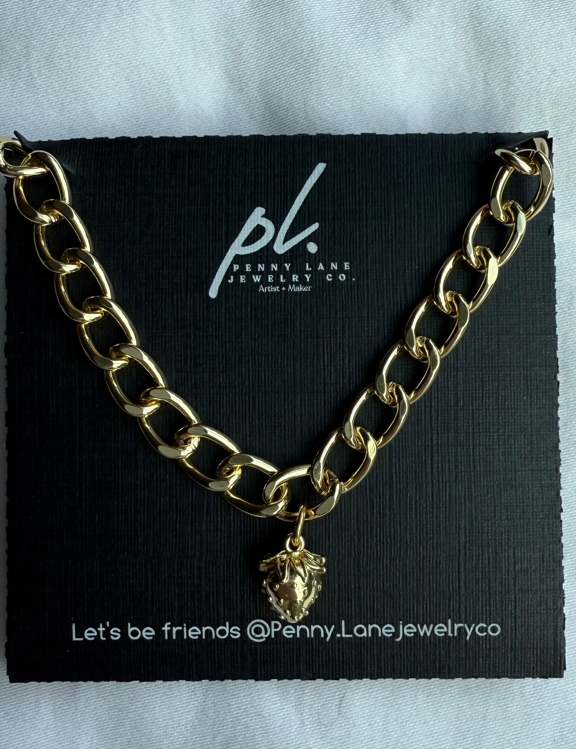 Gold chain necklace with a strawberry pendant on a Penny Lane Jewelry Co. card.