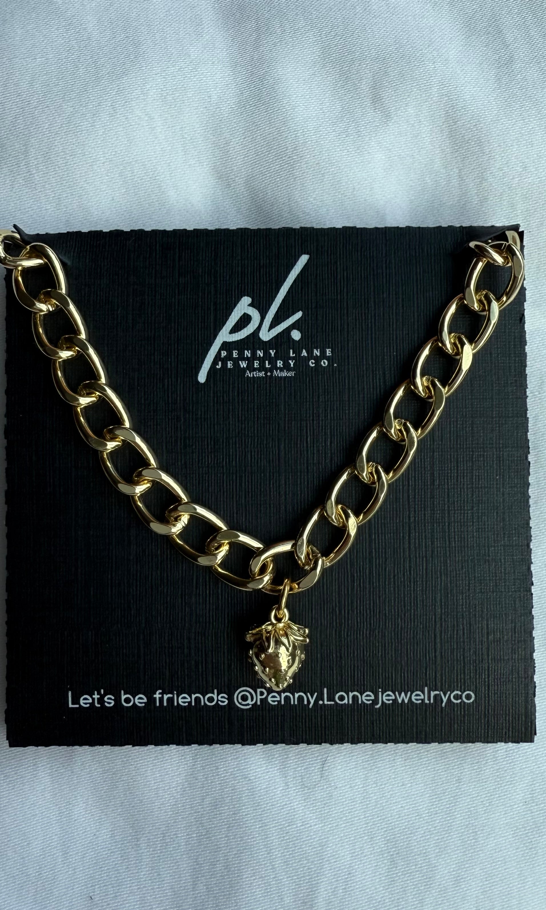 Gold chain necklace with a strawberry pendant on a Penny Lane Jewelry Co. card.