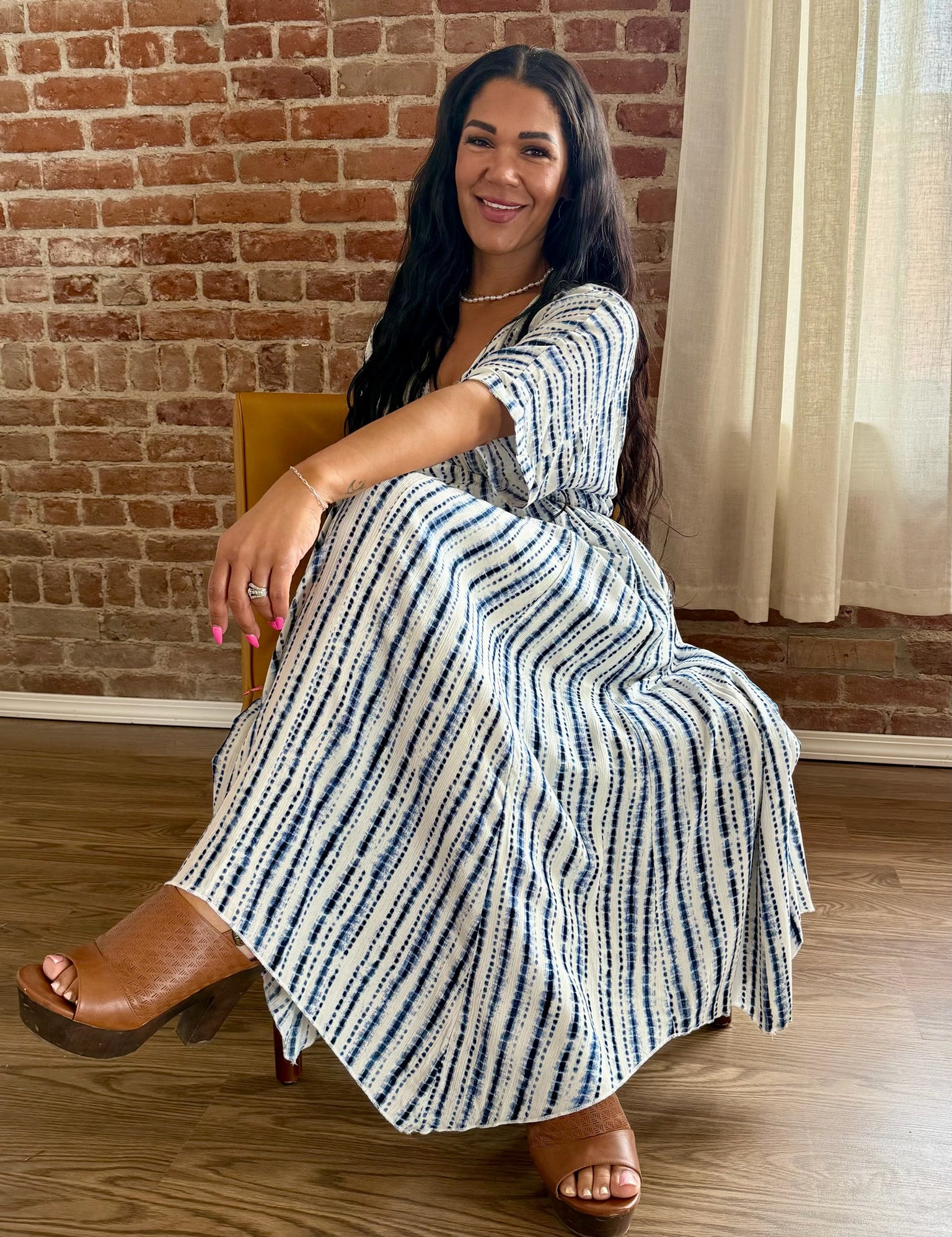 Woman in a striped dress sitting on a chair against a brick wall.