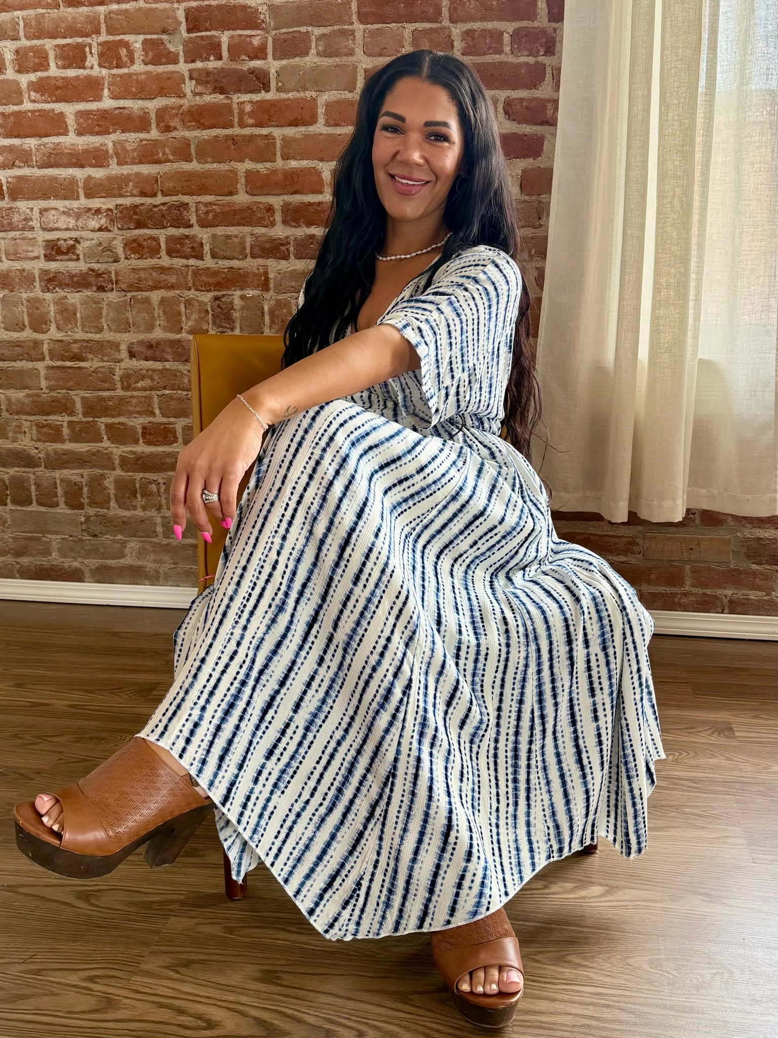Woman in a striped dress sitting on a chair against a brick wall.