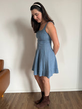 Woman wearing a blue dress standing against a plain wall.