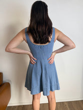 Person wearing a blue dress standing against a plain wall.