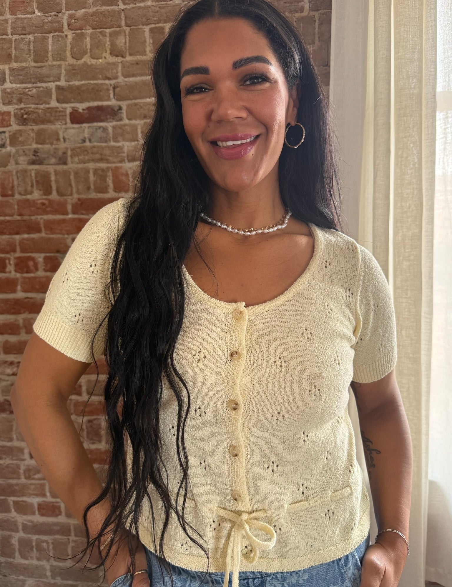 Woman wearing a light-colored cardigan standing in front of a brick wall.