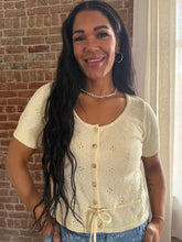Woman wearing a light-colored cardigan standing in front of a brick wall.