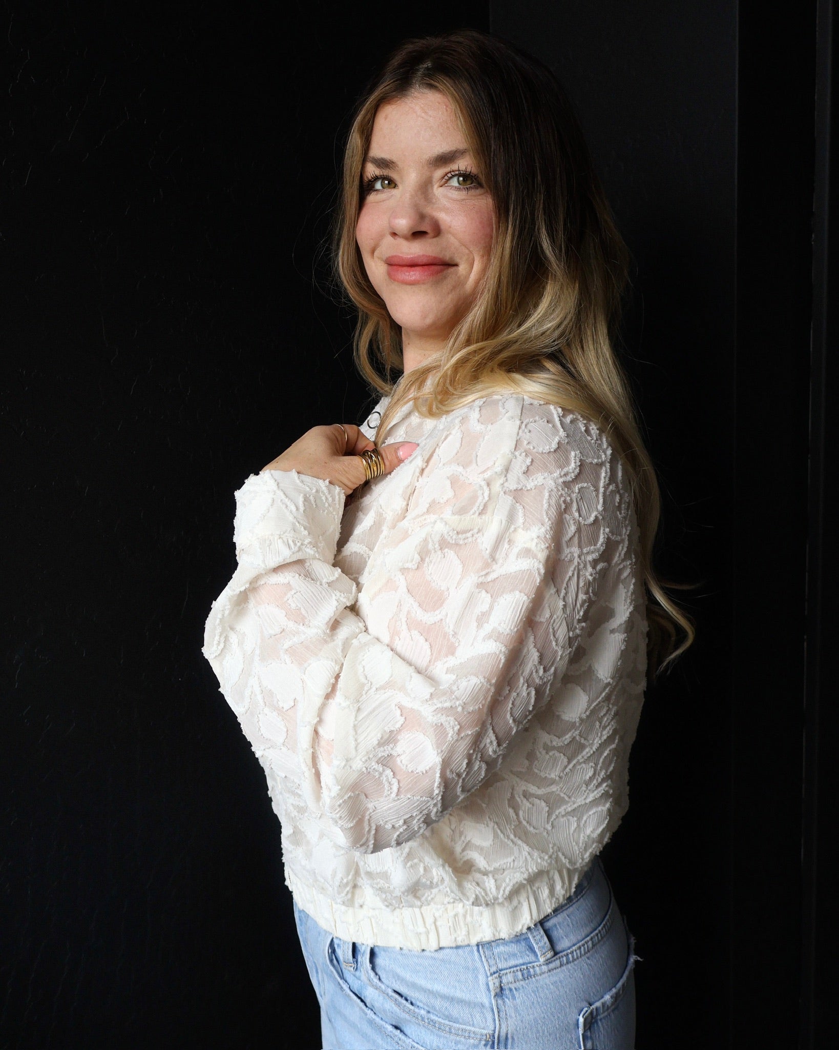 Woman wearing a white lace top and blue jeans against a black background