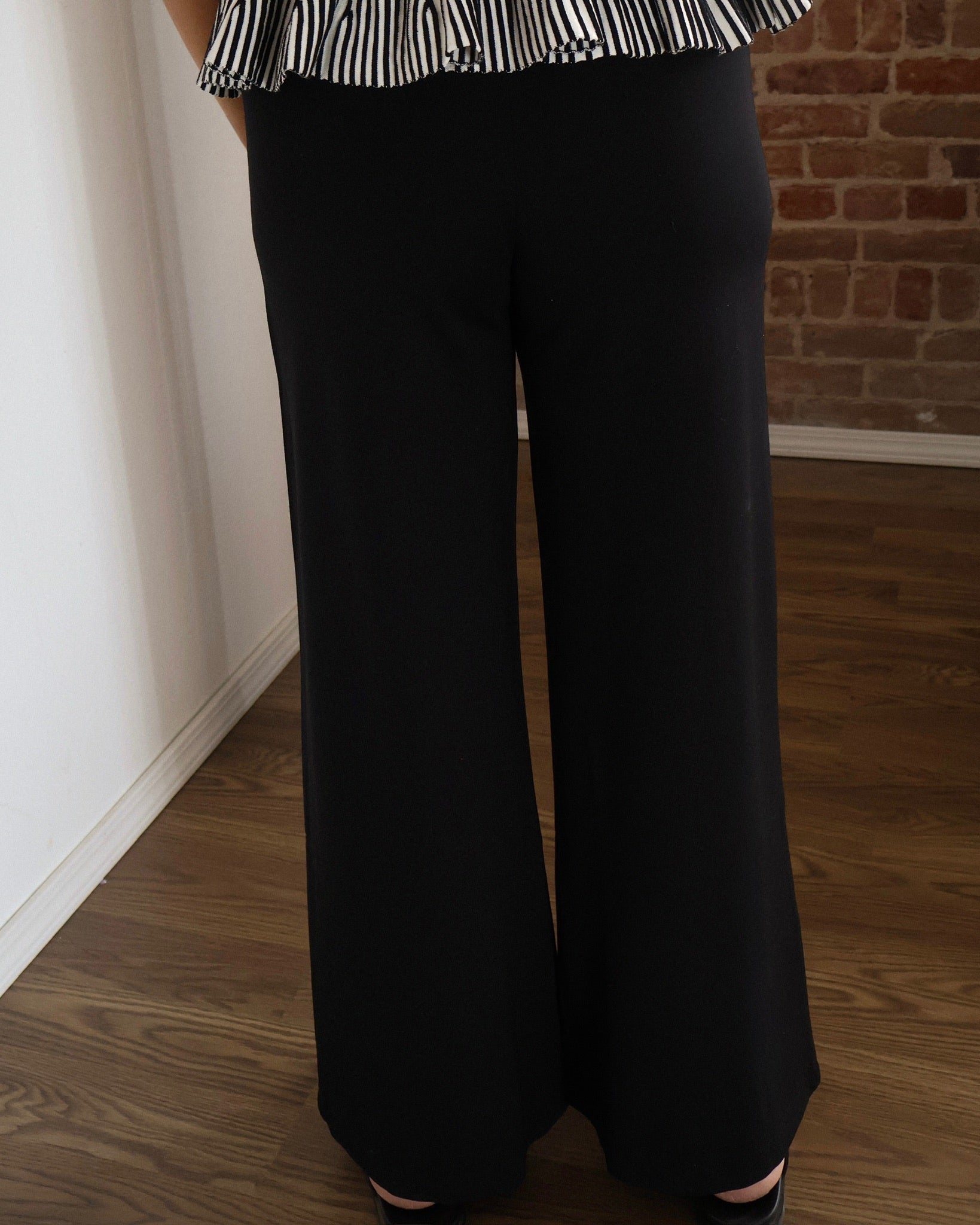 Person wearing black wide-leg pants and a striped top against a brick wall.
