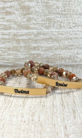 Two beaded bracelets with engraved names on a textured surface