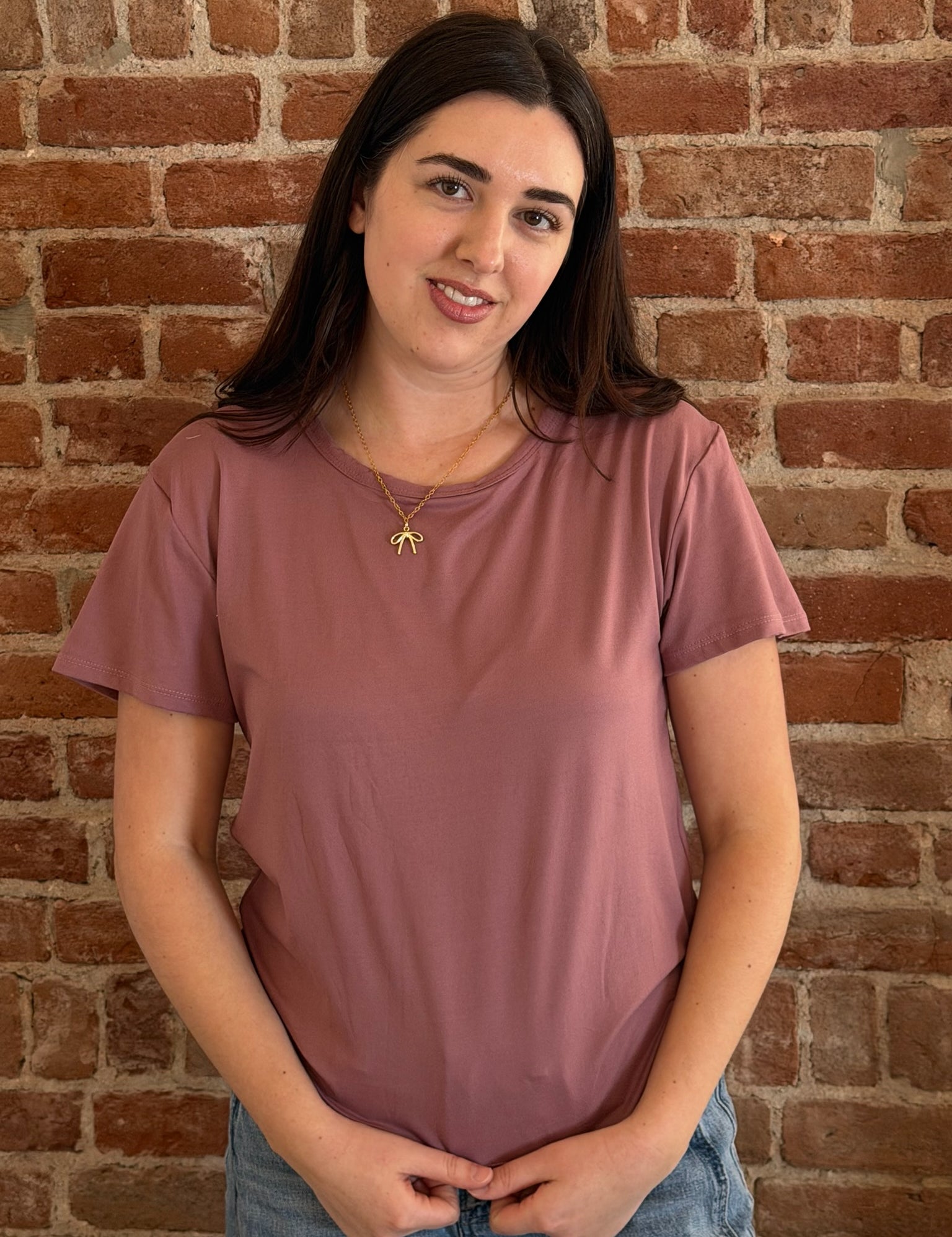 Woman wearing a mauve t-shirt standing against a brick wall