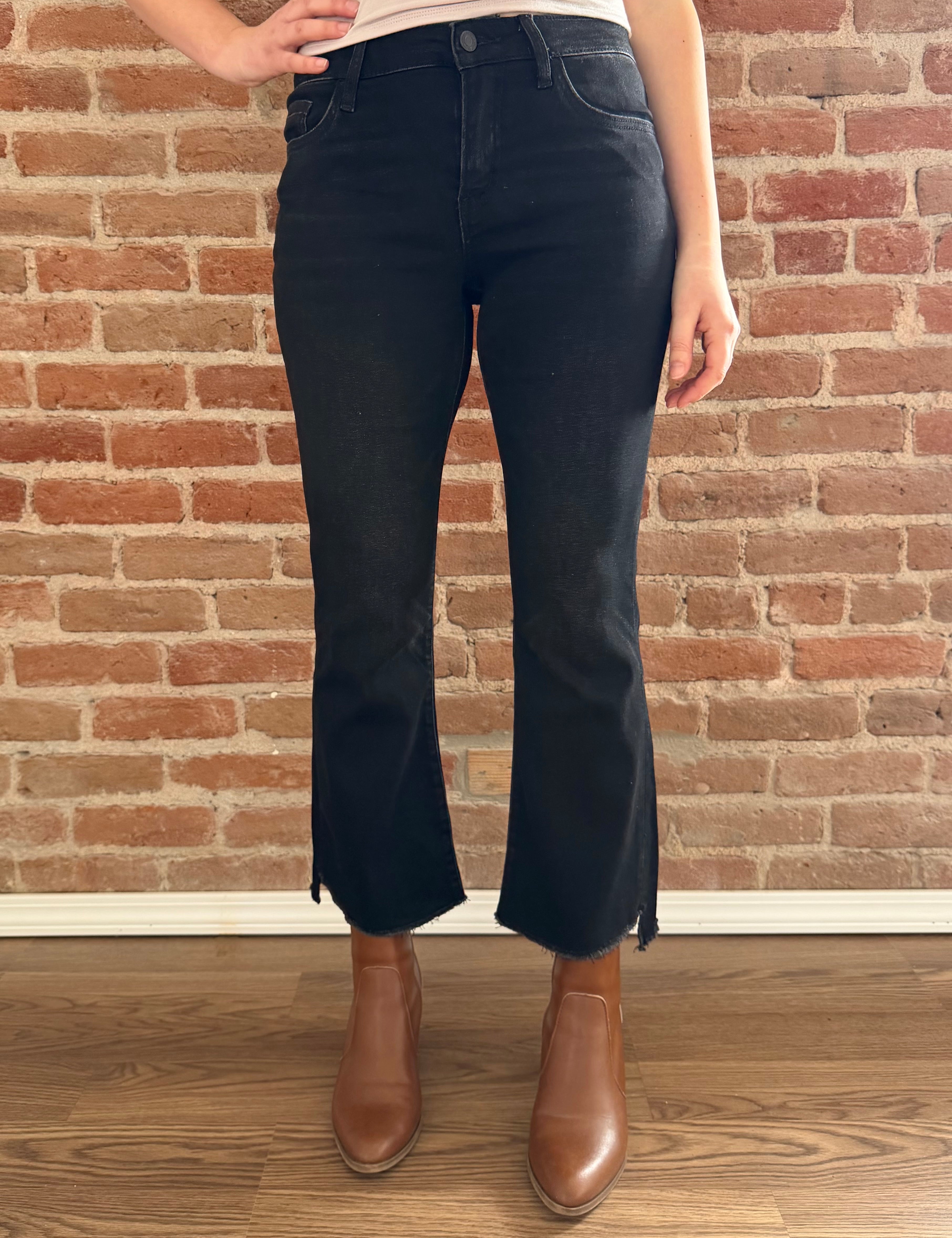 Person wearing black flared jeans and brown boots standing against a brick wall.