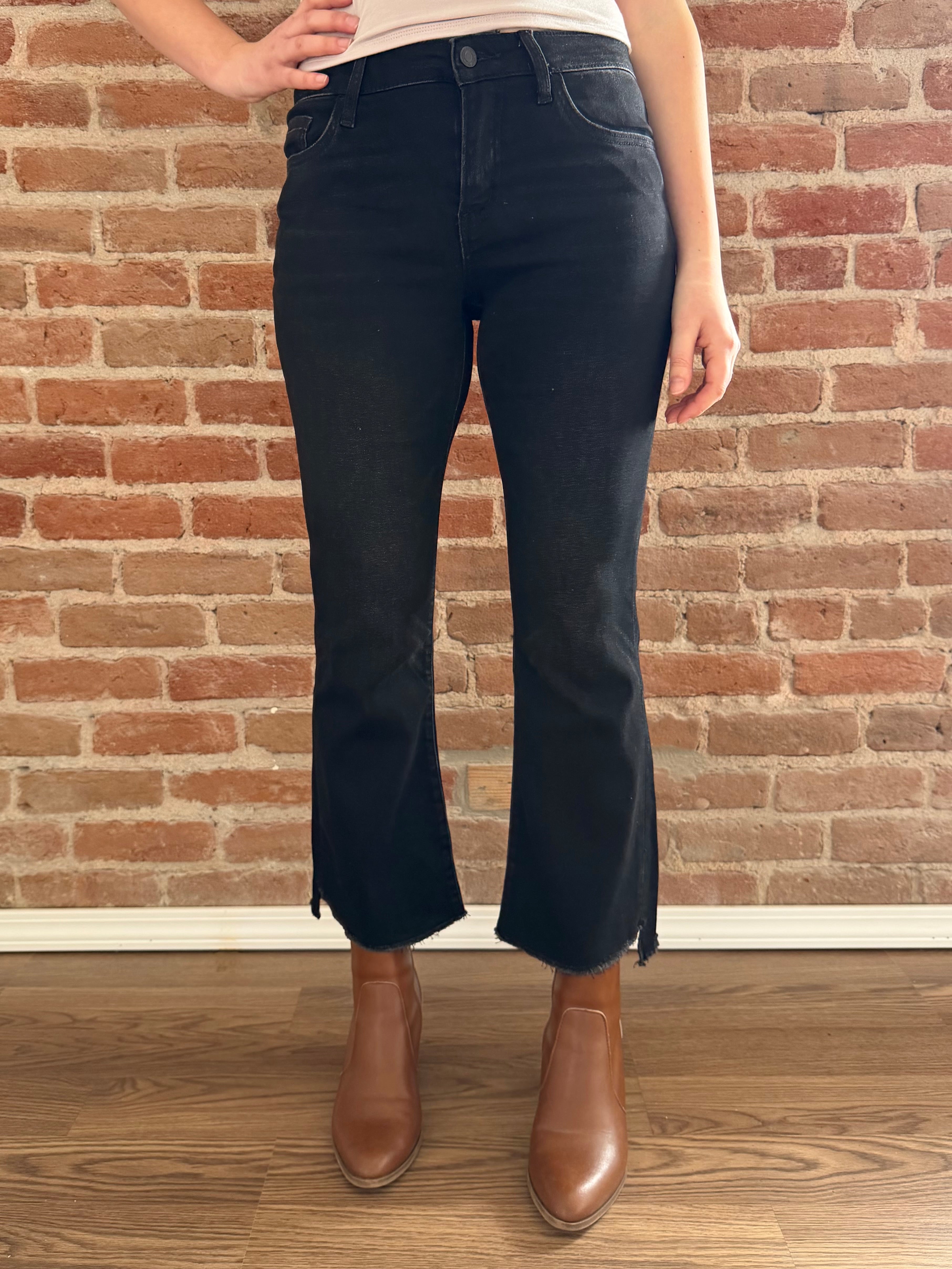 Person wearing black flared jeans and brown boots standing against a brick wall.