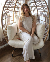 Woman sitting in a round wicker chair with white cushions indoors.